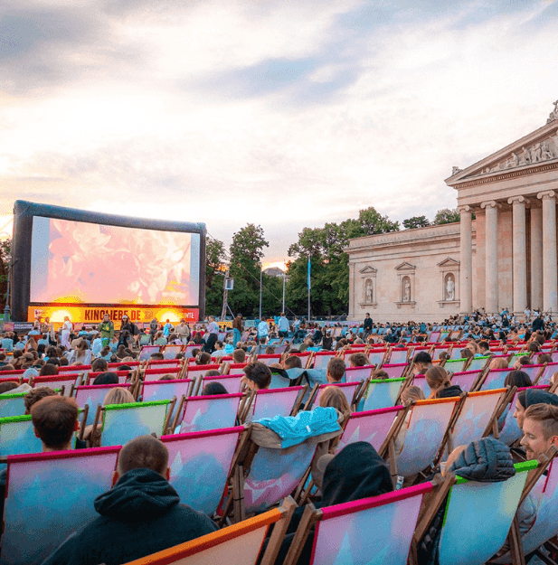 Crowd watches an outdoor movie on a giant screen before a grand classical building.