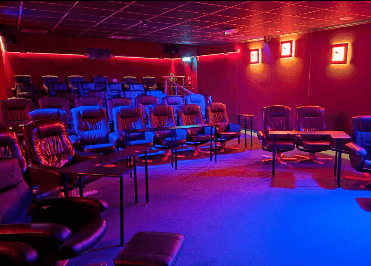 Dark room with rows of comfortable chairs illuminated by red and blue lights.
